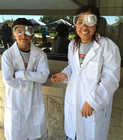 Two children wearing lab coats and protective eyewear 